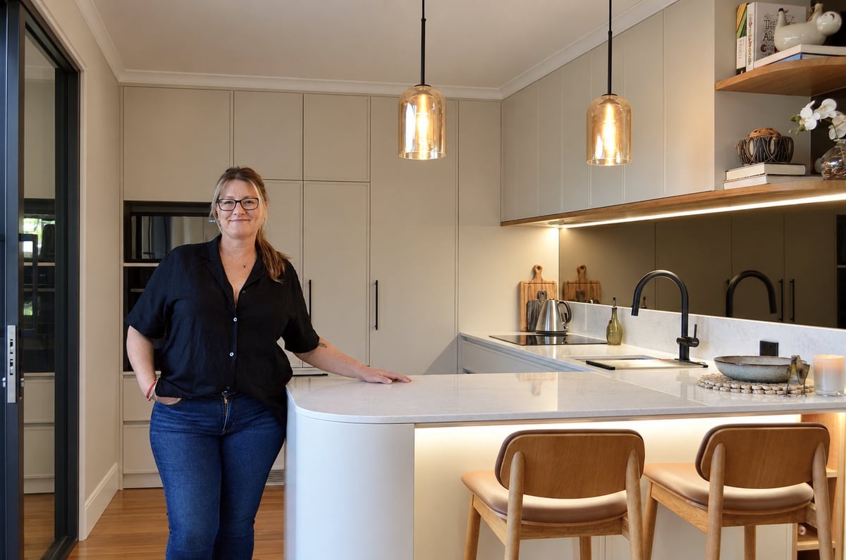 Lucy standing at a modern kitchen counter with pendant lights and bar seating inside one of her completed cabinetry projects